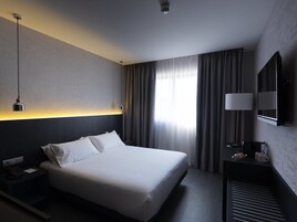 A hotel room with a large bed, bedside table, lamp, and a mirror.