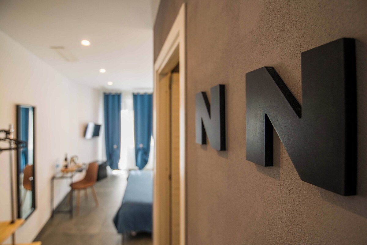 A modern interior with a hallway leading to a dining area. There are two large black letters 'NN' on the wall.