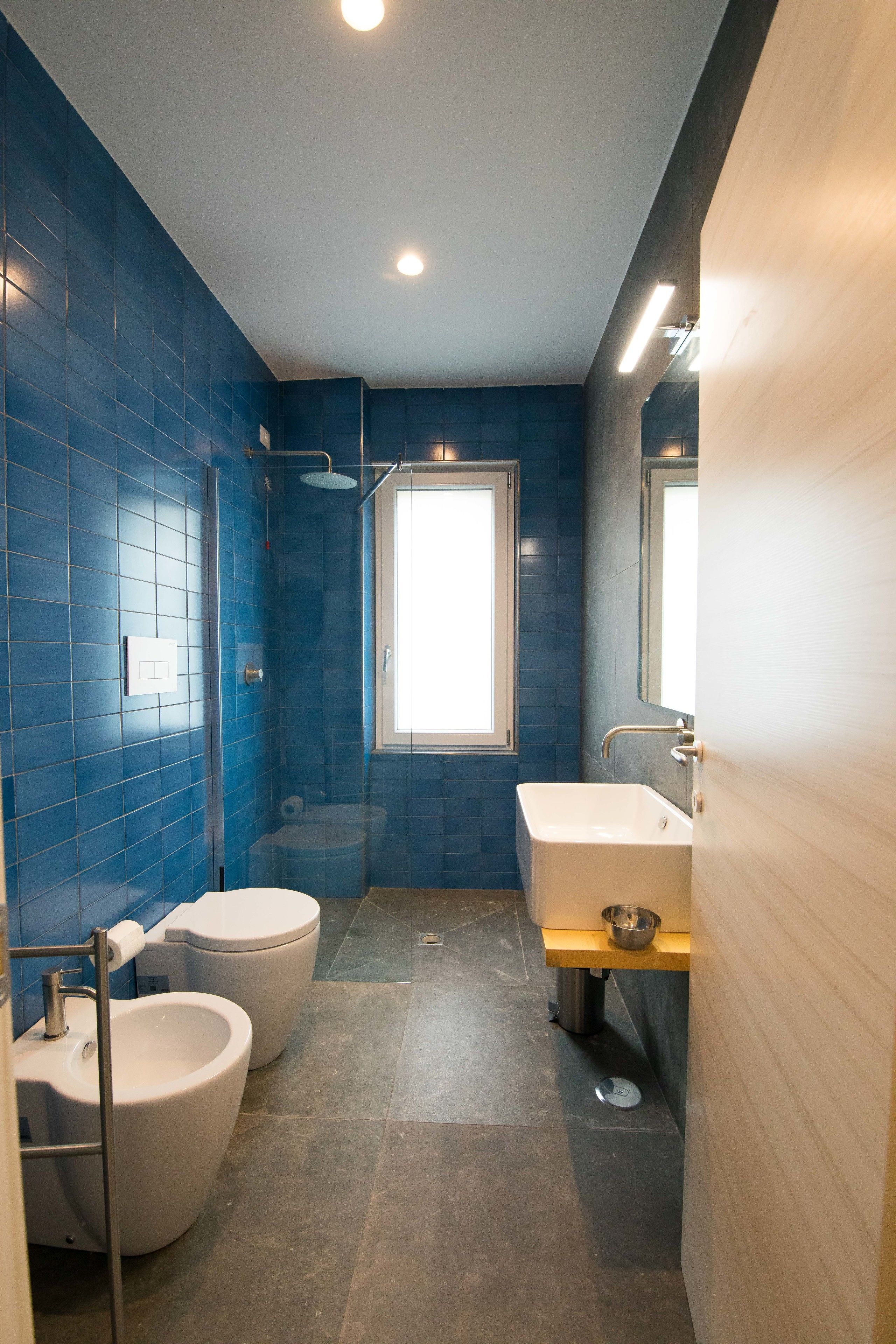 Un baño con azulejos azules, inodoro blanco, bidé, bañera y lavabo con espejo.
