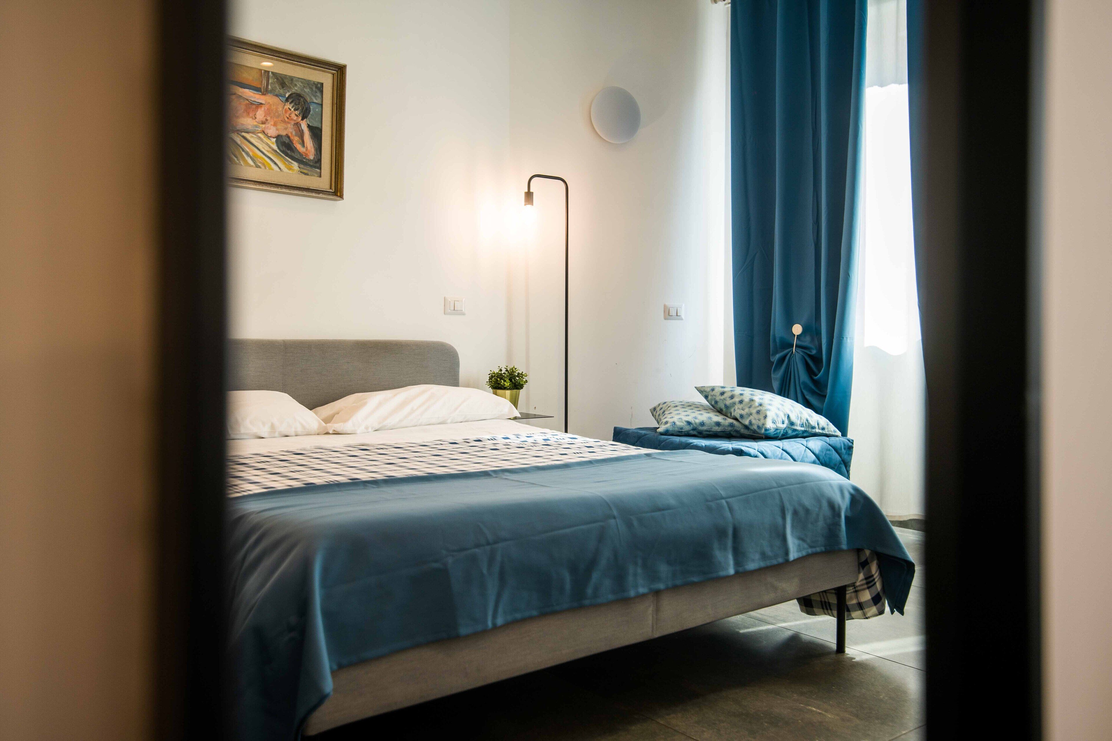 A bedroom with a bed, a bedside table, a lamp, and a window with curtains.