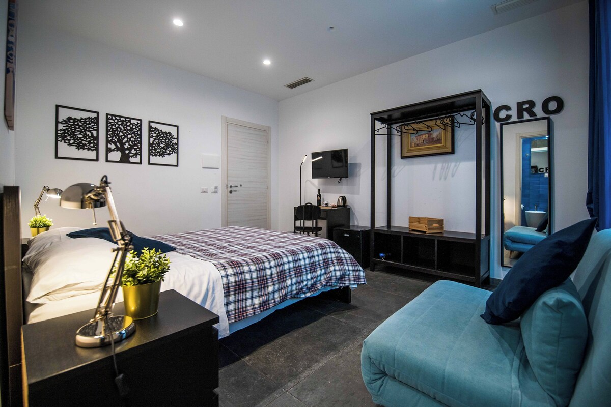 A modern bedroom with a bed, a desk, a chair, and a TV.