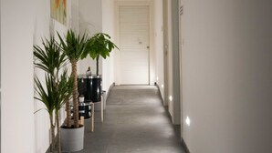 En smal hall med krukväxter, en dörr längst ner och infälld belysning.