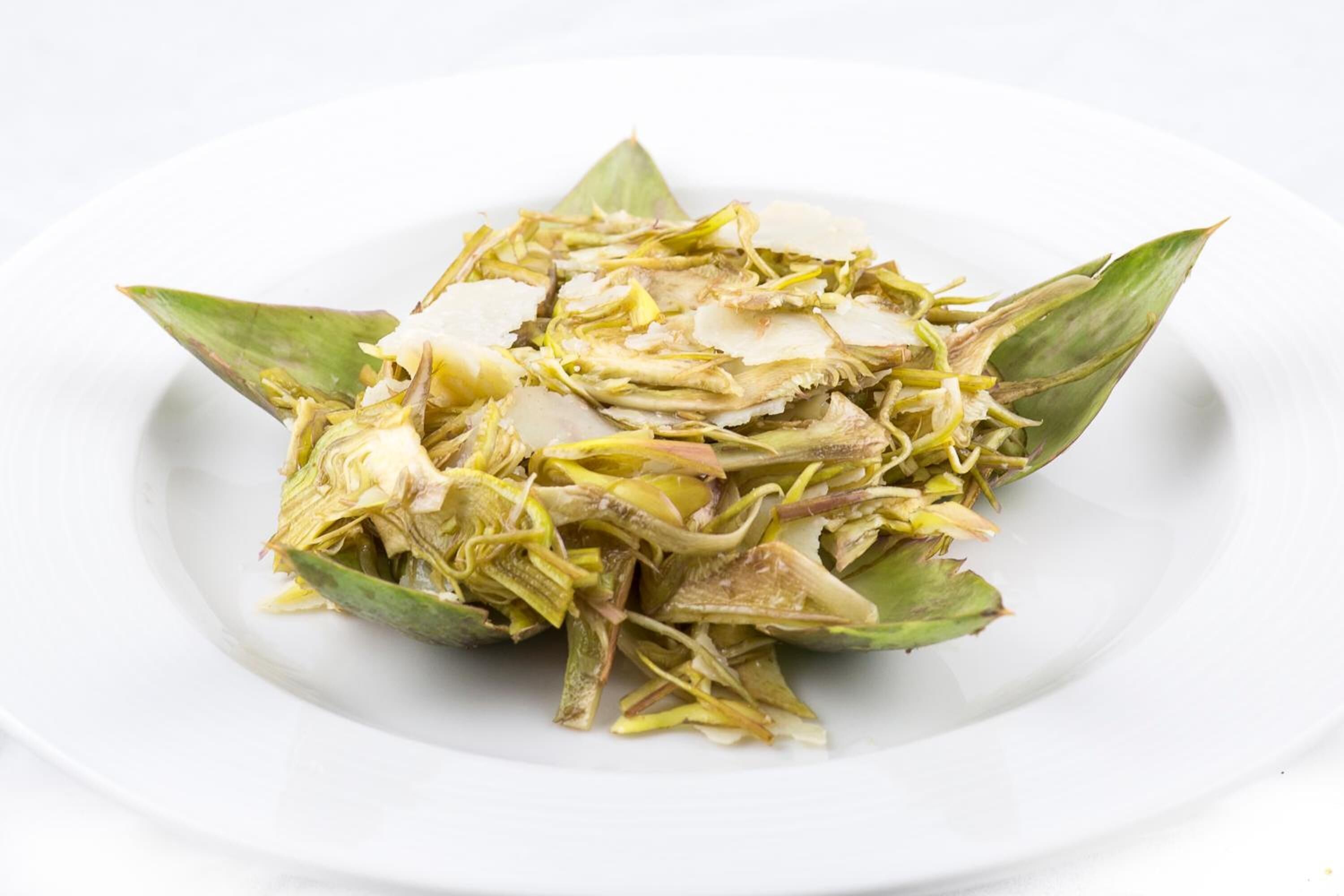 Un piatto bianco con un'insalata di verdure a foglia verde e verdure tagliate a fettine.