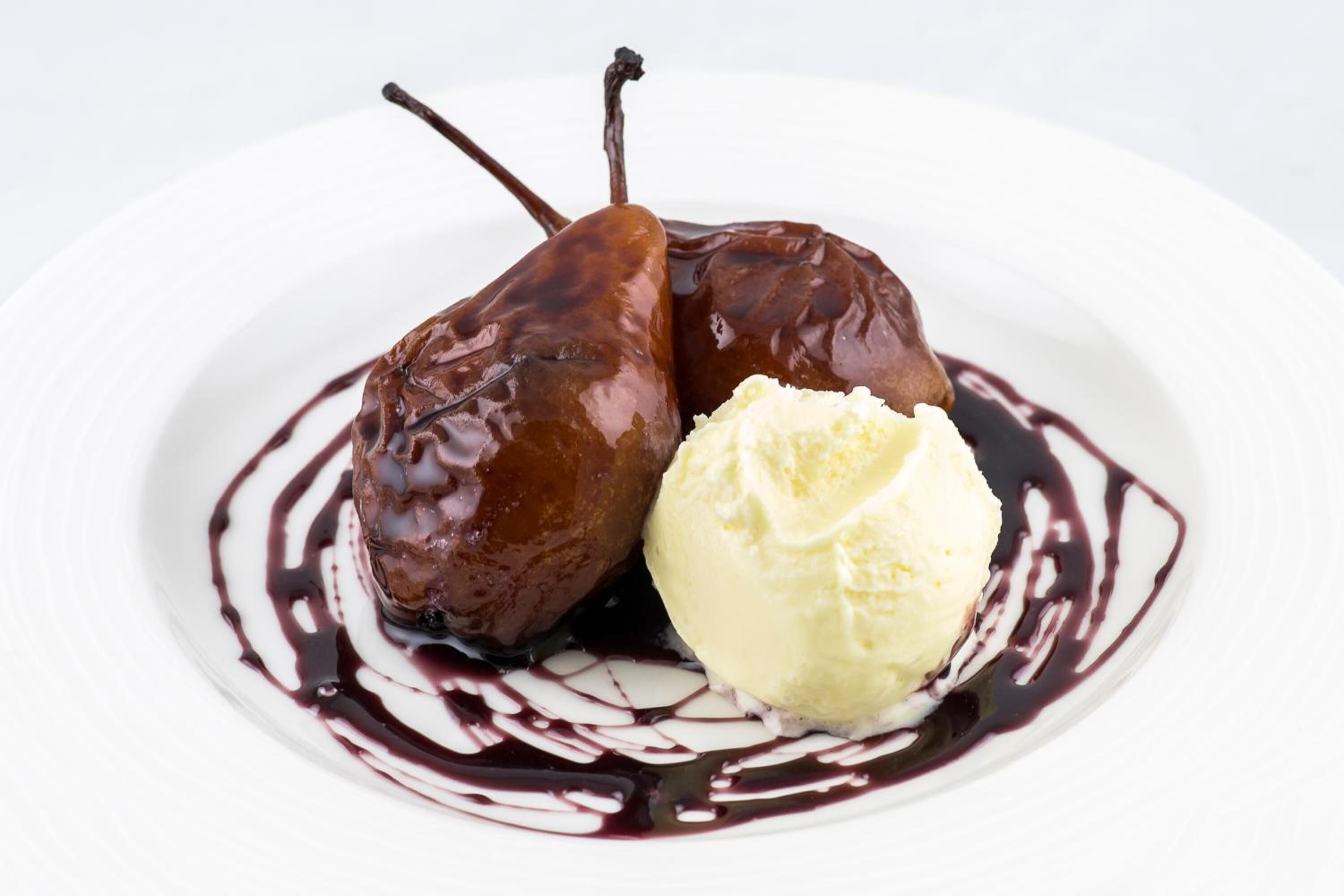 Un dessert con due pere al cioccolato e una pallina di gelato alla vaniglia su un piatto bianco.
