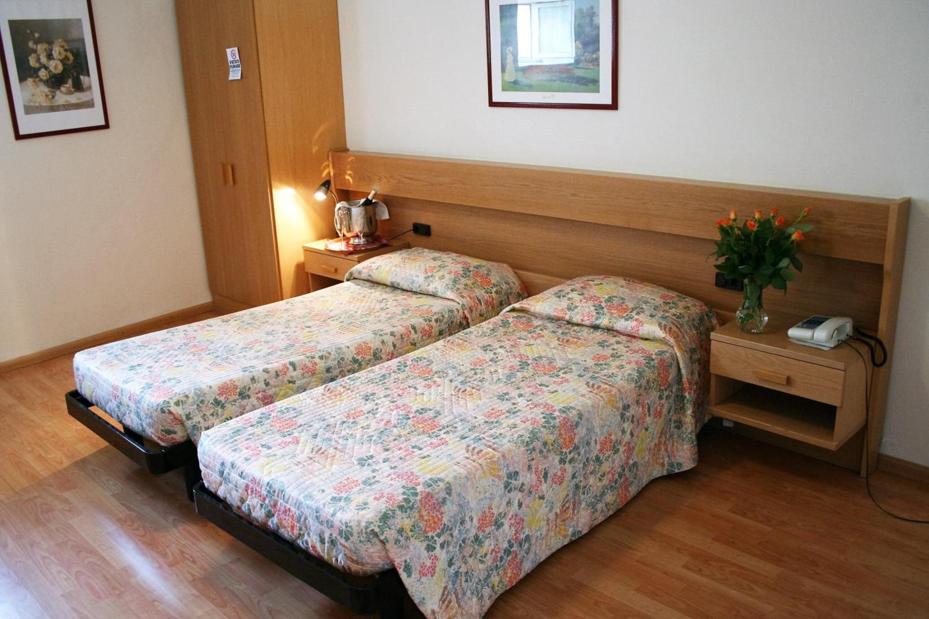 Un dormitorio con dos camas individuales, cabeceros de madera, mesitas de noche con lámparas, un aparador con teléfono y un armario de madera.