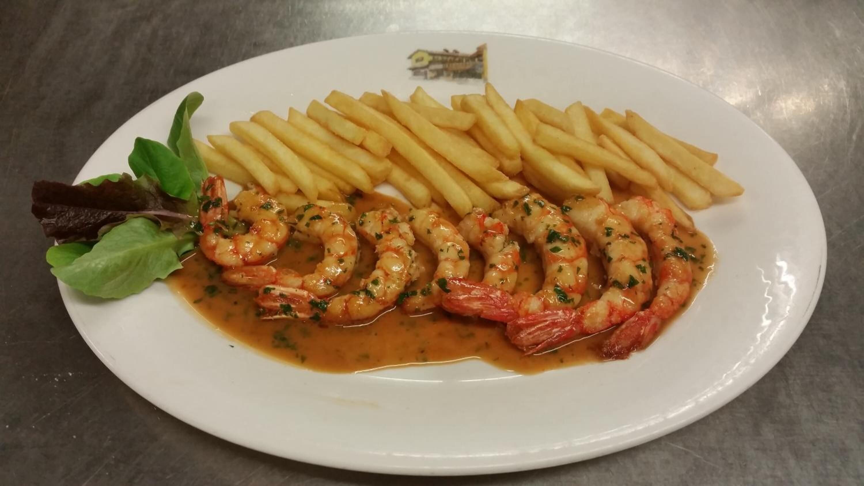 A plate with shrimp, fries, and a small salad on a white plate.