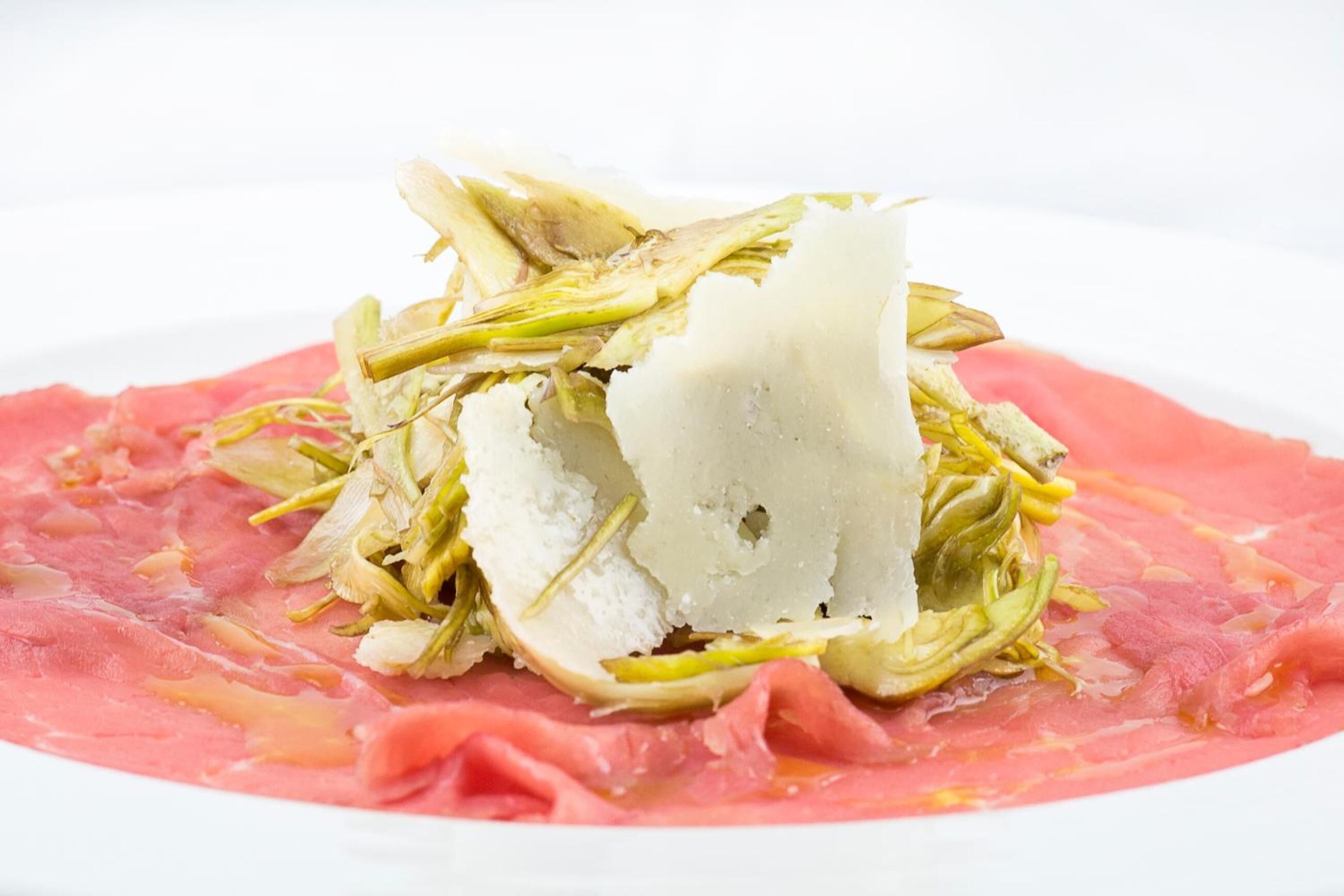 A dish with a white creamy substance, green leafy vegetables, and pink meat on a white plate.