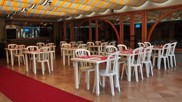 Un restaurante con sillas blancas y caminos de mesa rojos, ventanas amplias y una alfombra roja que conduce al área de estar.