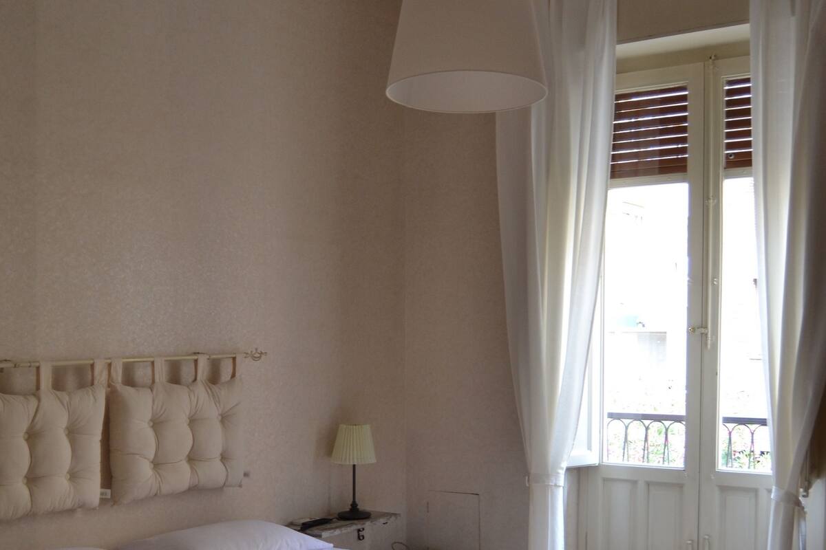 A hotel room with a large bed, a bedside table with a lamp, and a window with curtains.