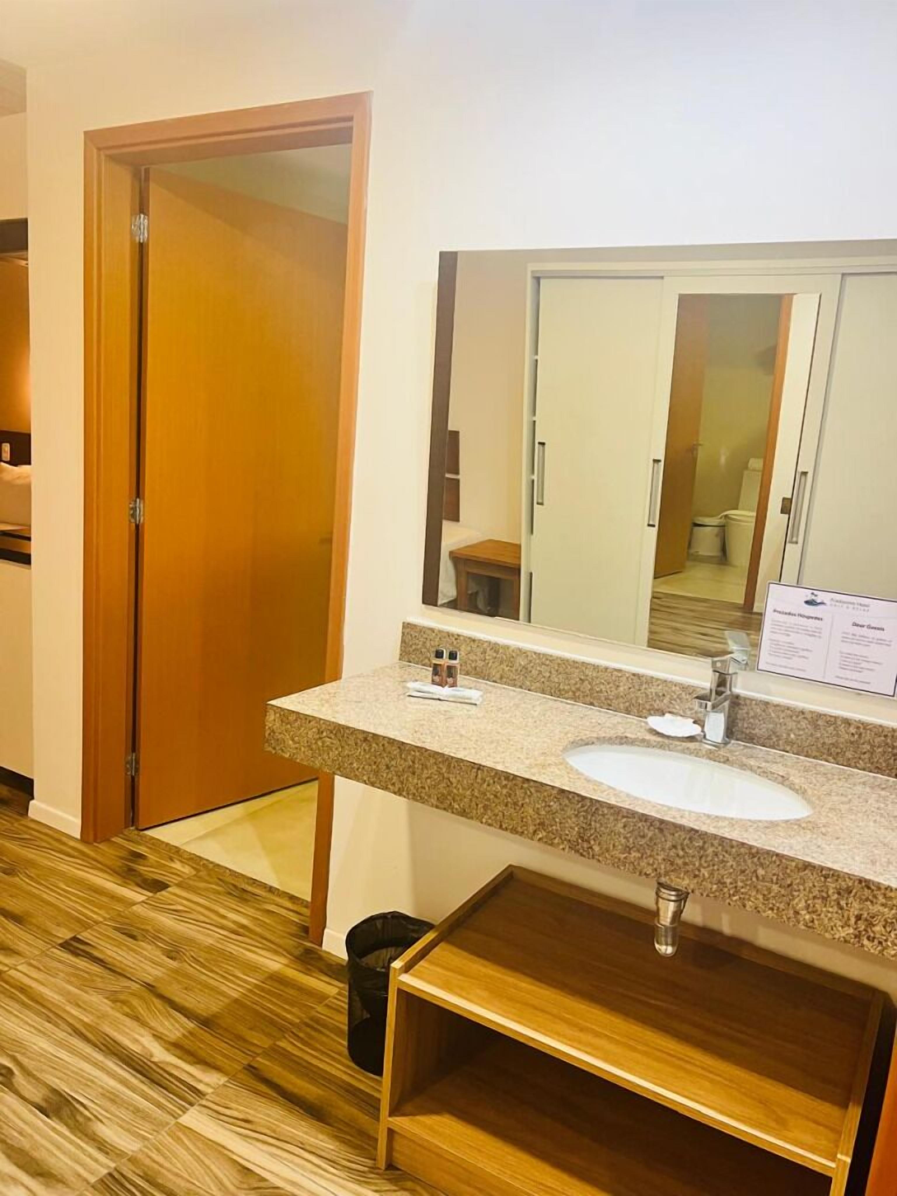 Ein Hotelbad mit Holzboden, einem Waschbecken mit Granitplatte, einem Spiegel und einem Holzschrank unter dem Waschbecken.