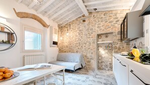 A compact kitchen with stone walls, a dining area with a table and oranges, and a bed in the corner. - Giglio Oro by Mmega (Florence)