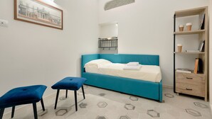 A bedroom with a blue bed, two blue stools, a wooden nightstand, and a framed picture on the wall. - Giglio Oro by Mmega (Florence)