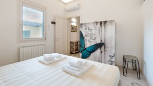 A hotel room with a large bed, a window with blinds, a wall-mounted air conditioner, and a butterfly artwork. - Giglio Oro by Mmega (Florence)