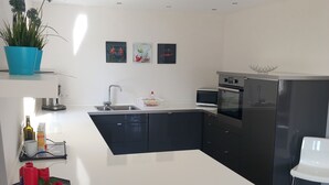 Une cuisine moderne dotée d’un îlot central, de meubles de couleur sombre, de plans de travail blancs et d’un réfrigérateur en acier inoxydable.