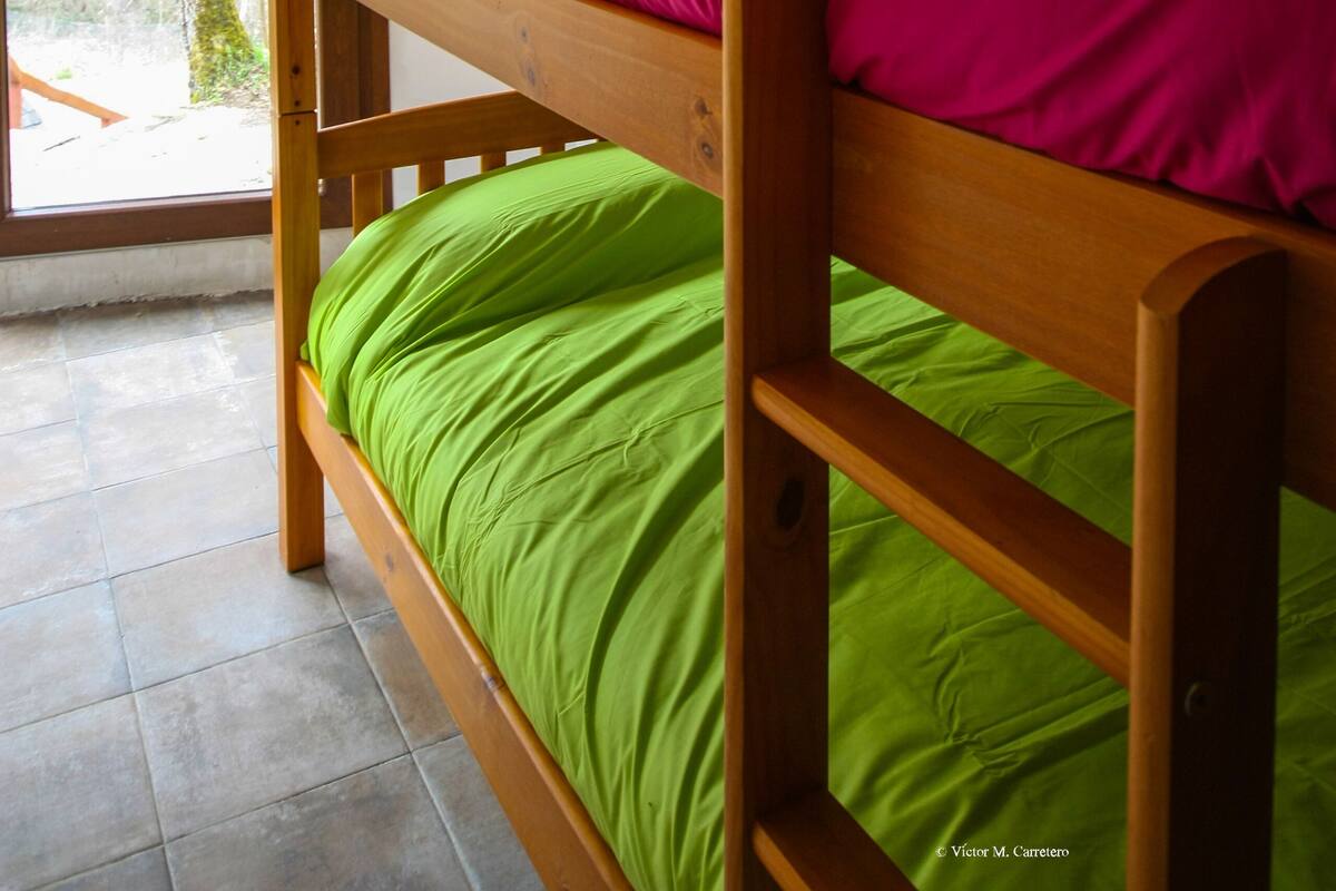Ein Stockbett mit grün-pink gestreuter Bettwäsche in einem Zimmer mit Fenster.