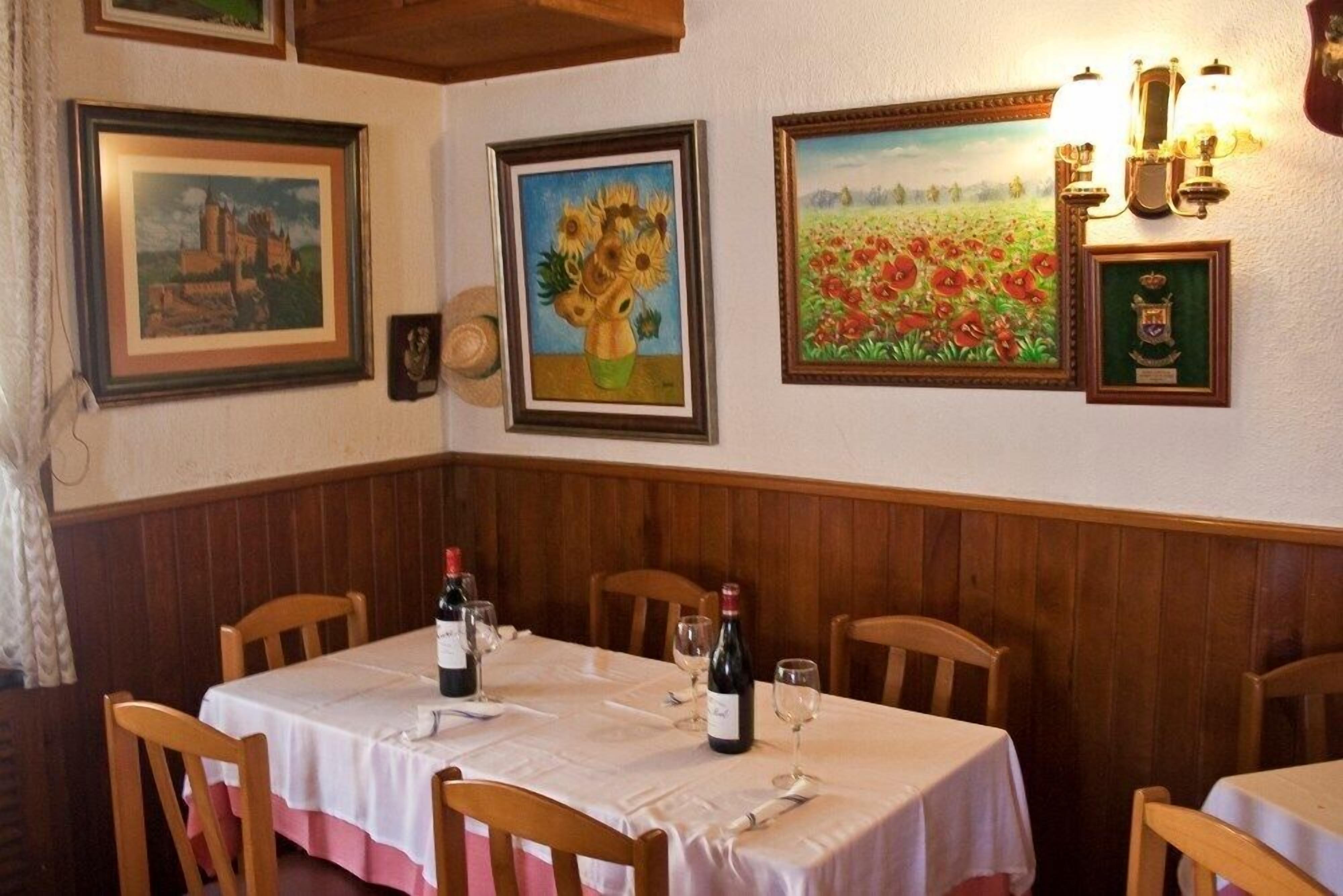 Ein Essbereich mit Holzwänden, einem gedeckten Tisch mit Weingläsern und Flaschen sowie gerahmten Bildern an den Wänden.