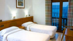 Une chambre d’hôtel avec deux lits, une tête de lit en bois, un tableau au mur, une fenêtre avec des rideaux et une vue sur la ville.