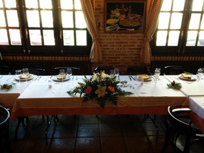 A restaurant with a long table set for dining, featuring a floral centerpiece and a painting on the wall. - Hostal La Maya (Cercedilla)