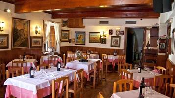 Un restaurant amb taules i cadires de fusta, estovalls blancs i quadres a les parets.