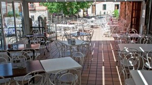 Un café en plein air avec des tables et des chaises en métal blanc, disposées sur une terrasse carrelée.