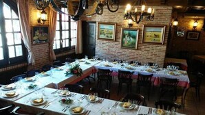 Un restaurant avec de longues tables disposées pour les repas, agrémenté d’un mur en briques et d’œuvres d’art encadrées.