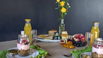 Ein Esstisch mit verschiedenen Speisen, darunter Pfannkuchen, Obst und eine Vase mit gelben Blumen.