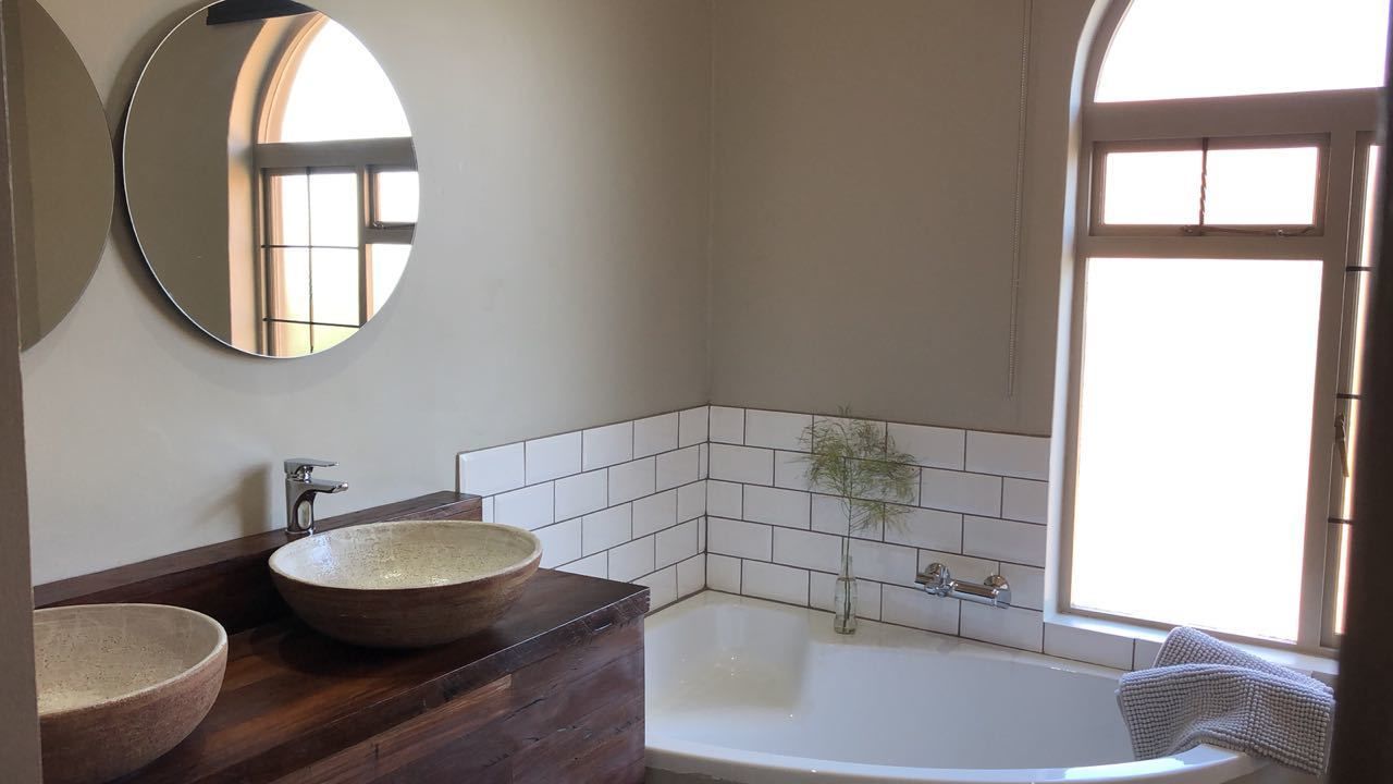 A bathroom with two ceramic sinks, a freestanding bathtub, a mirror, and a window with natural light.