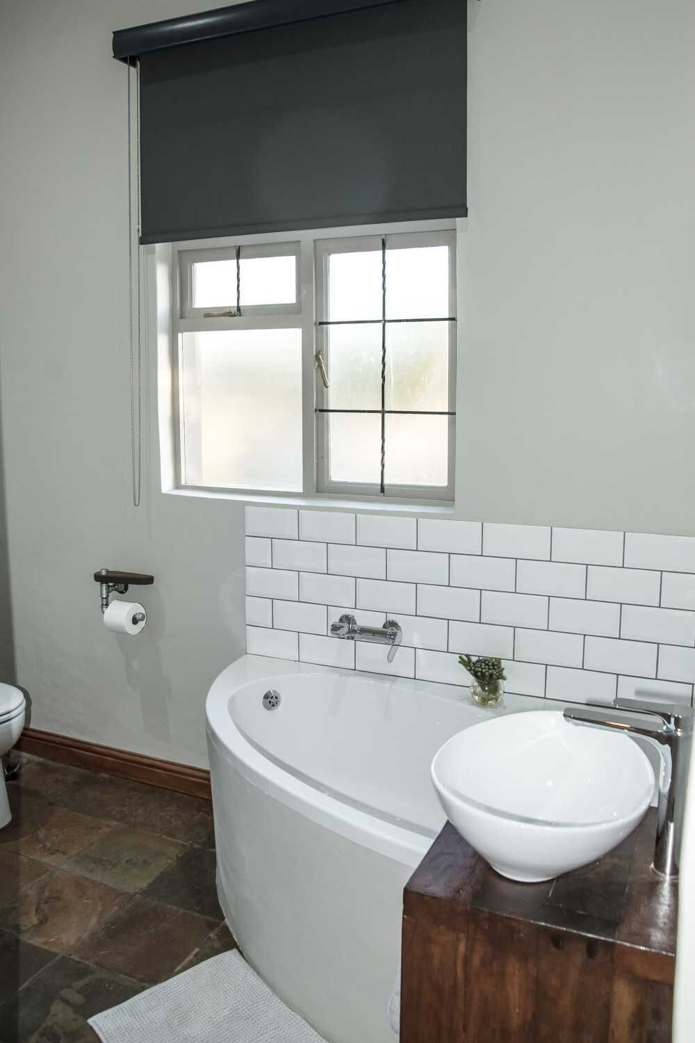 Un baño con bañera, inodoro, ventana con vidrio esmerilado y toallero.