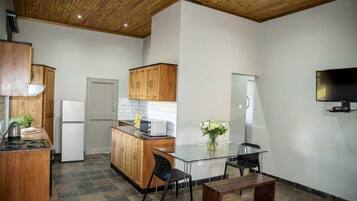 Una cocina compacta con armarios de madera, un refrigerador, una estufa y un comedor con mesa y sillas de vidrio.