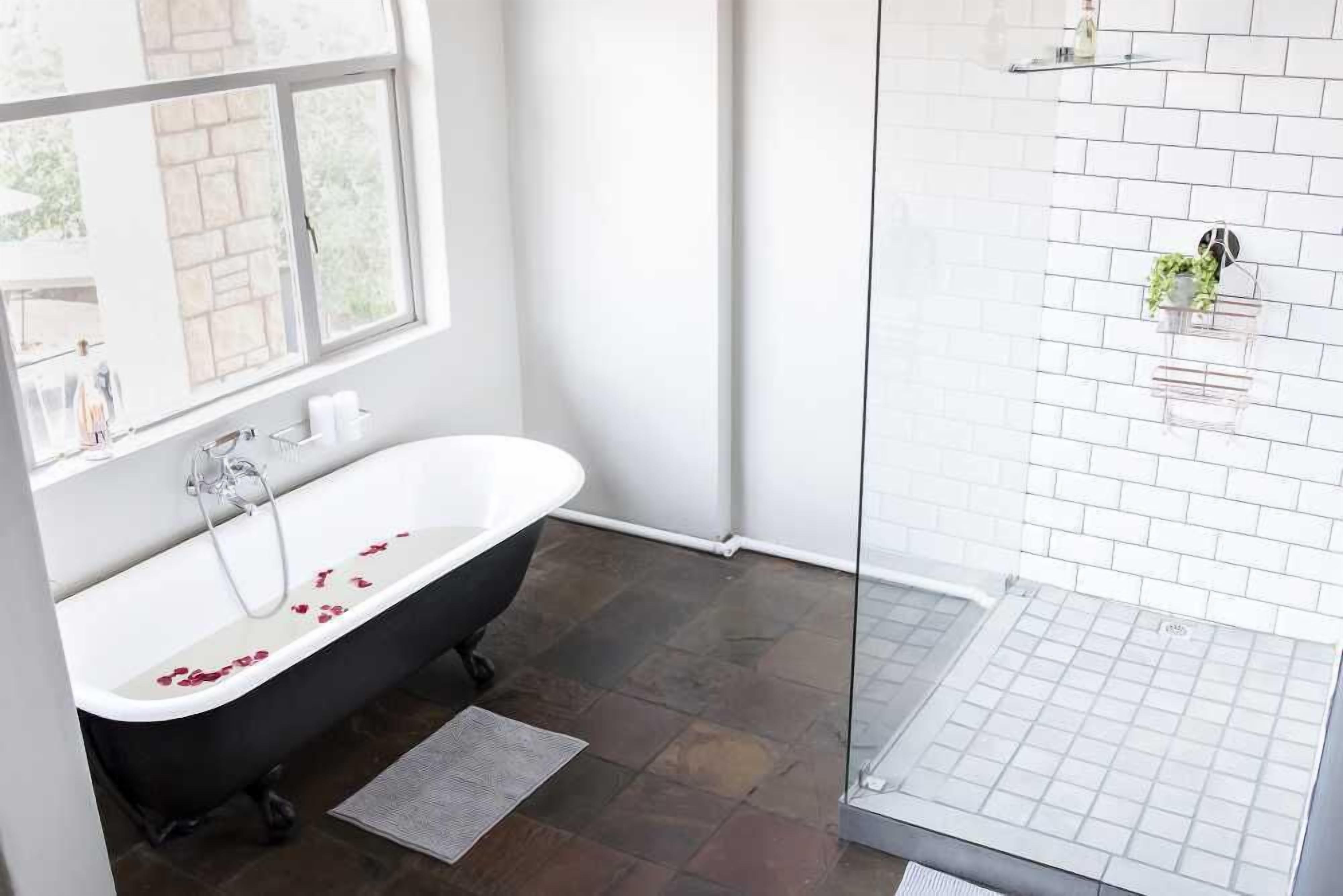 A bathroom with a freestanding bathtub, a glass shower enclosure, and a window with a view of the outside.
