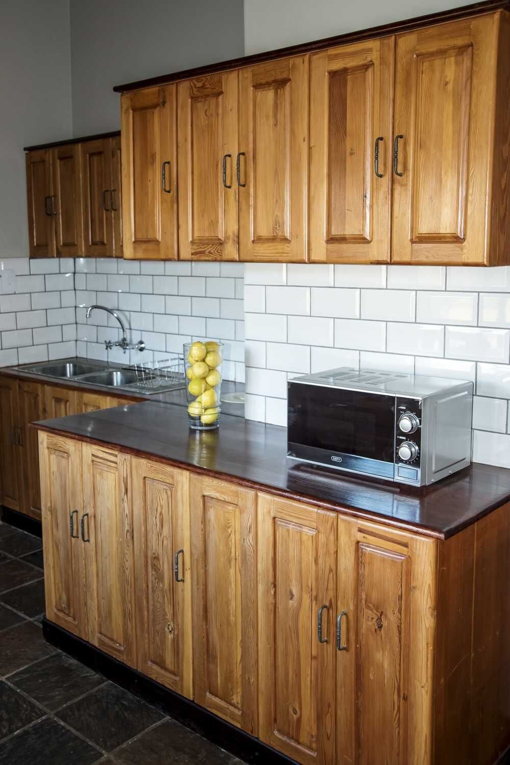 A kitchen with wooden cabinets, a stainless steel sink, and a microwave on the countertop.