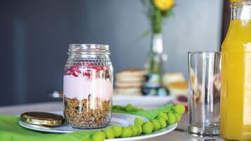A breakfast setting with a glass jar of layered yogurt and granola, a glass of orange juice, and a green fruit garnish on a plate.