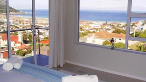 Quarto de hotel com uma grande janela que oferece vista para uma cidade costeira e o mar.