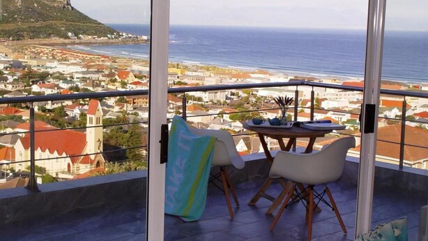 Varanda com mesa e cadeiras, com vista para uma cidade costeira e o mar.