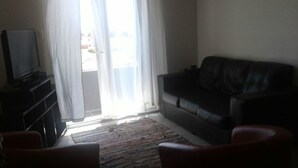 Ein Wohnzimmer mit einem schwarzen Ledersofa, einem Fernseher auf einem Schrank und einem gemusterten Teppich.