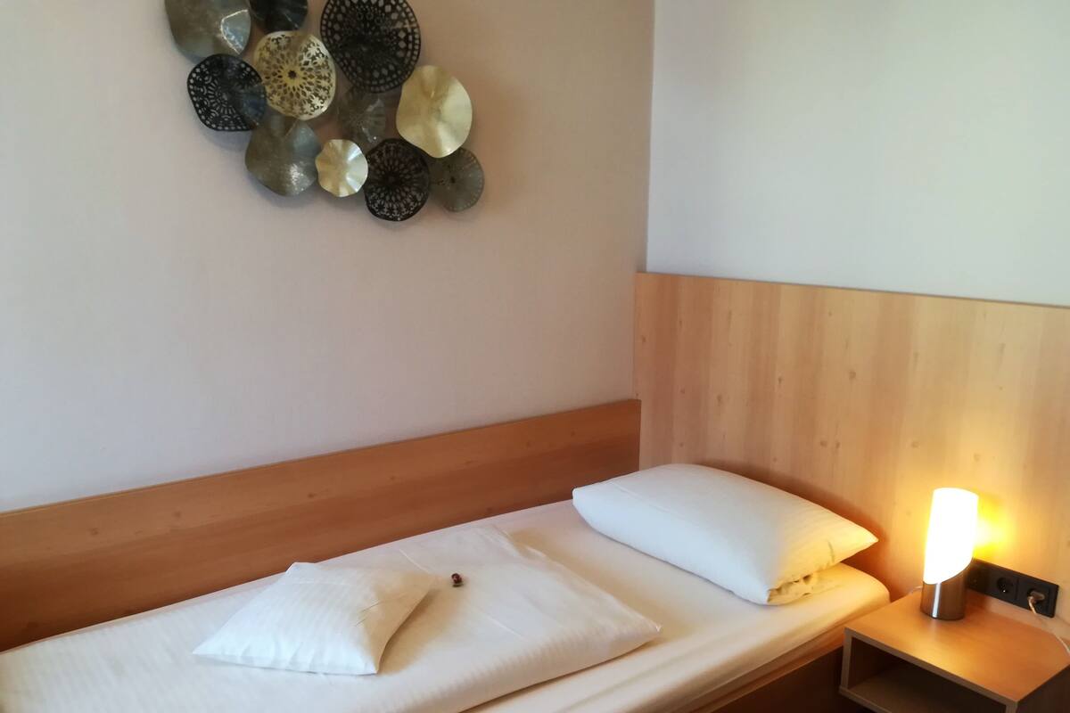 A single bed with white bedding, a wooden headboard, and a bedside table with a lamp.