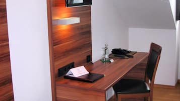 Et moderne kontor med et træskrivebord, en stol, et fladskærms-tv på væggen og et lille bord med et glas og en notesbog.