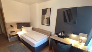 Una habitación de hotel moderna con cama, mesita de noche, escritorio, silla y televisor de pantalla plana montado en la pared.