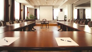 Una sala de conferencias con una larga mesa, sillas, una pantalla de proyector y una pizarra.