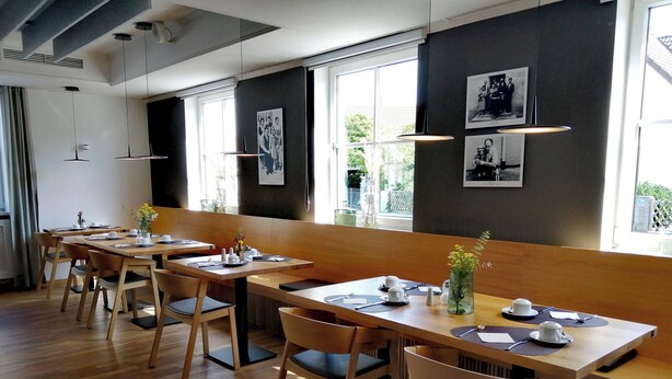 Un comedor moderno con mesas y sillas de madera, ventanas amplias y fotografías blanco y negro en las paredes.