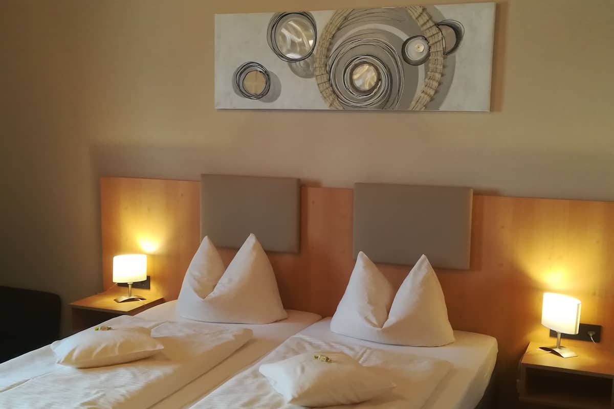 A hotel room with a double bed, two bedside tables with lamps, and a modern abstract painting on the wall.