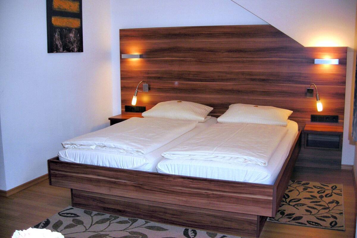 A double bed with a wooden headboard, two bedside tables with lamps, and a floral-patterned rug on the floor.