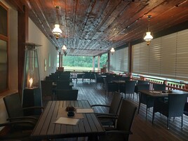 Un restaurante con mesas y sillas de madera, una chimenea y amplias ventanas con persianas.