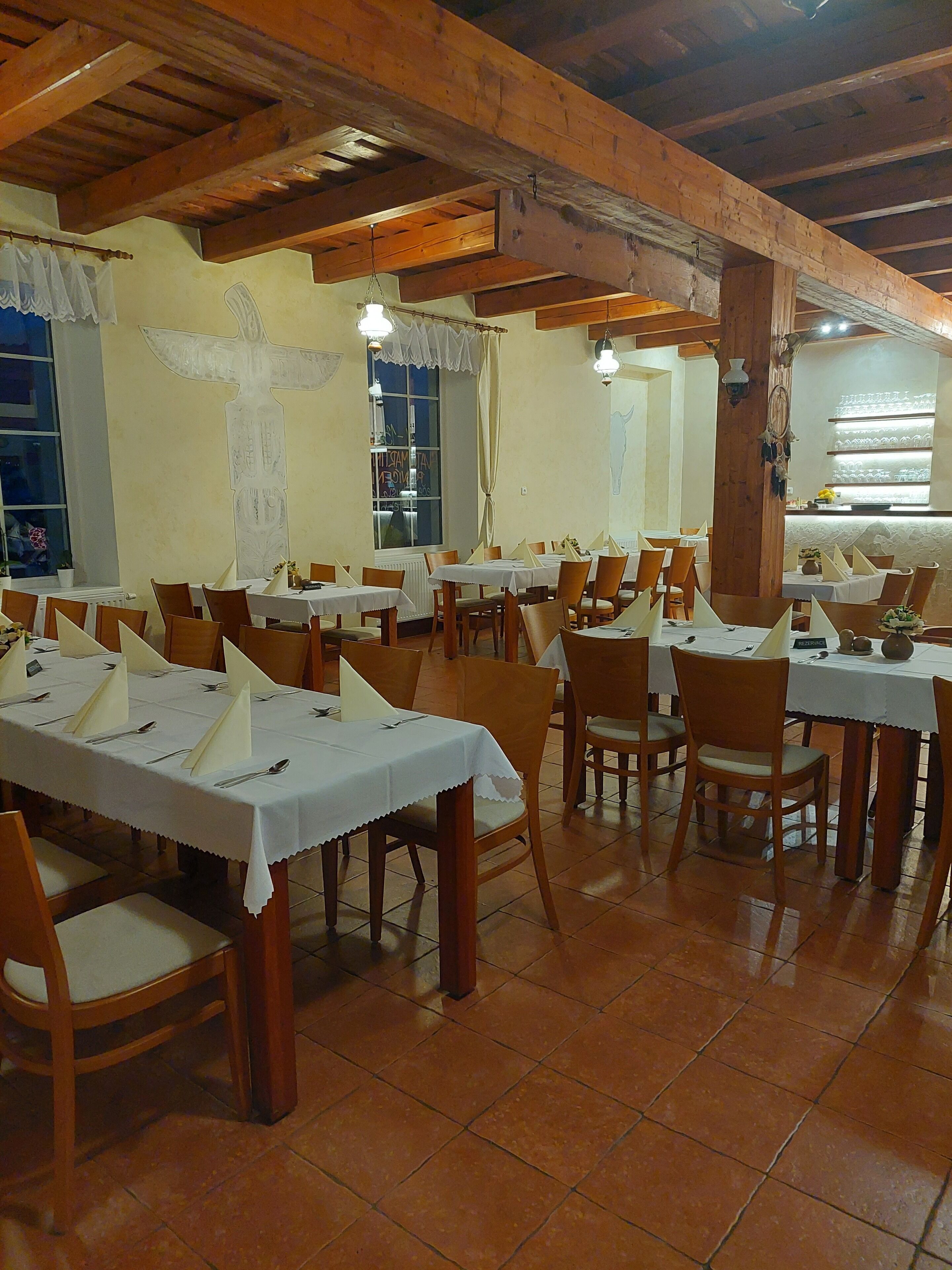 Un restaurant avec de nombreuses tables dressées, des poutres en bois au plafond et une grande fenêtre offrant une vue panoramique.