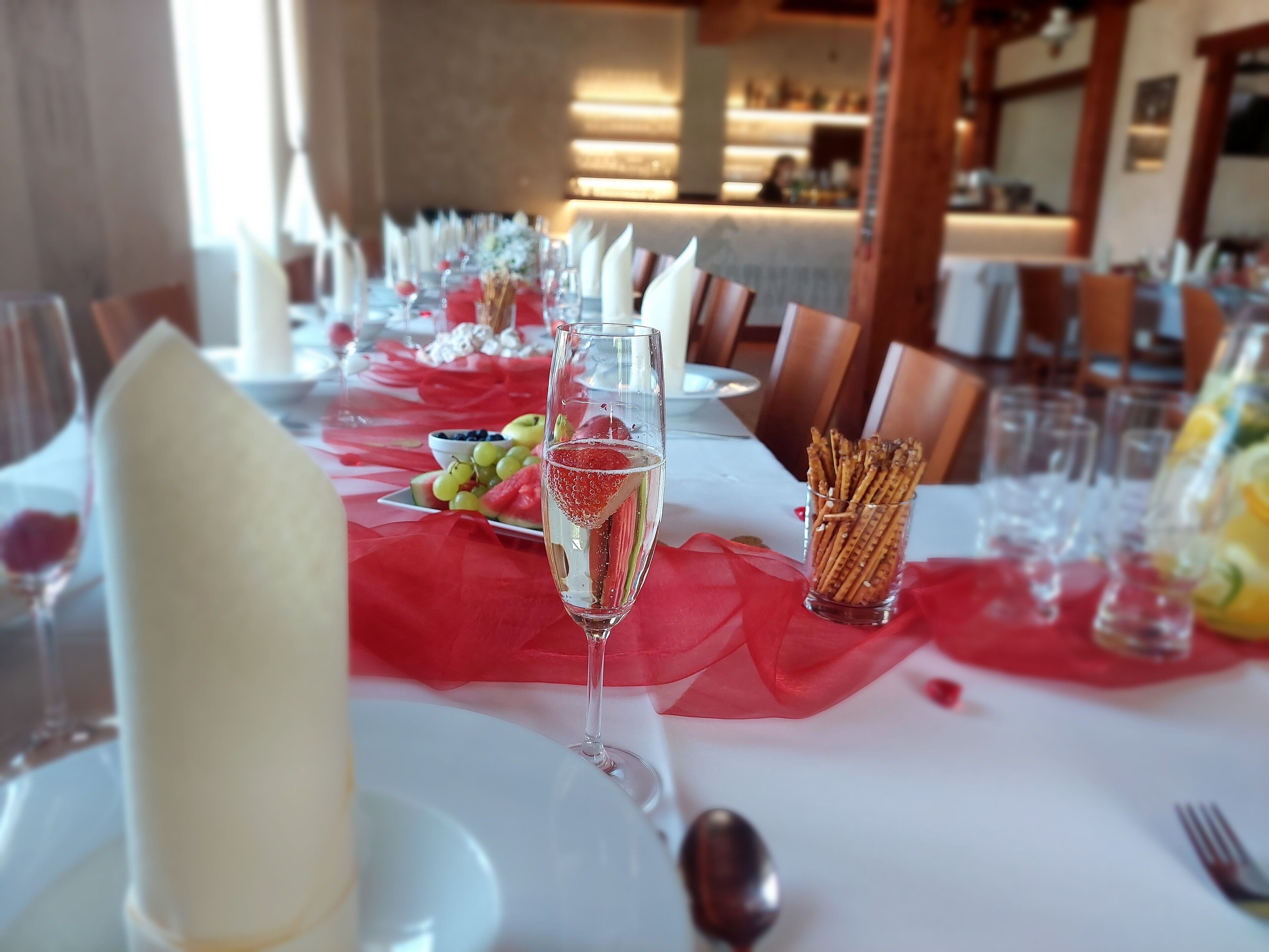 A dining table set with white plates, a glass of champagne, fruit, and pretzels.