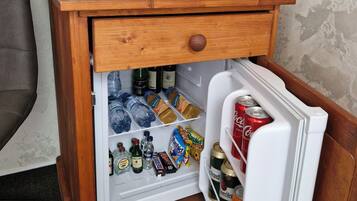 A compact refrigerator with a wooden exterior, containing various beverages, snacks, and bottled water.