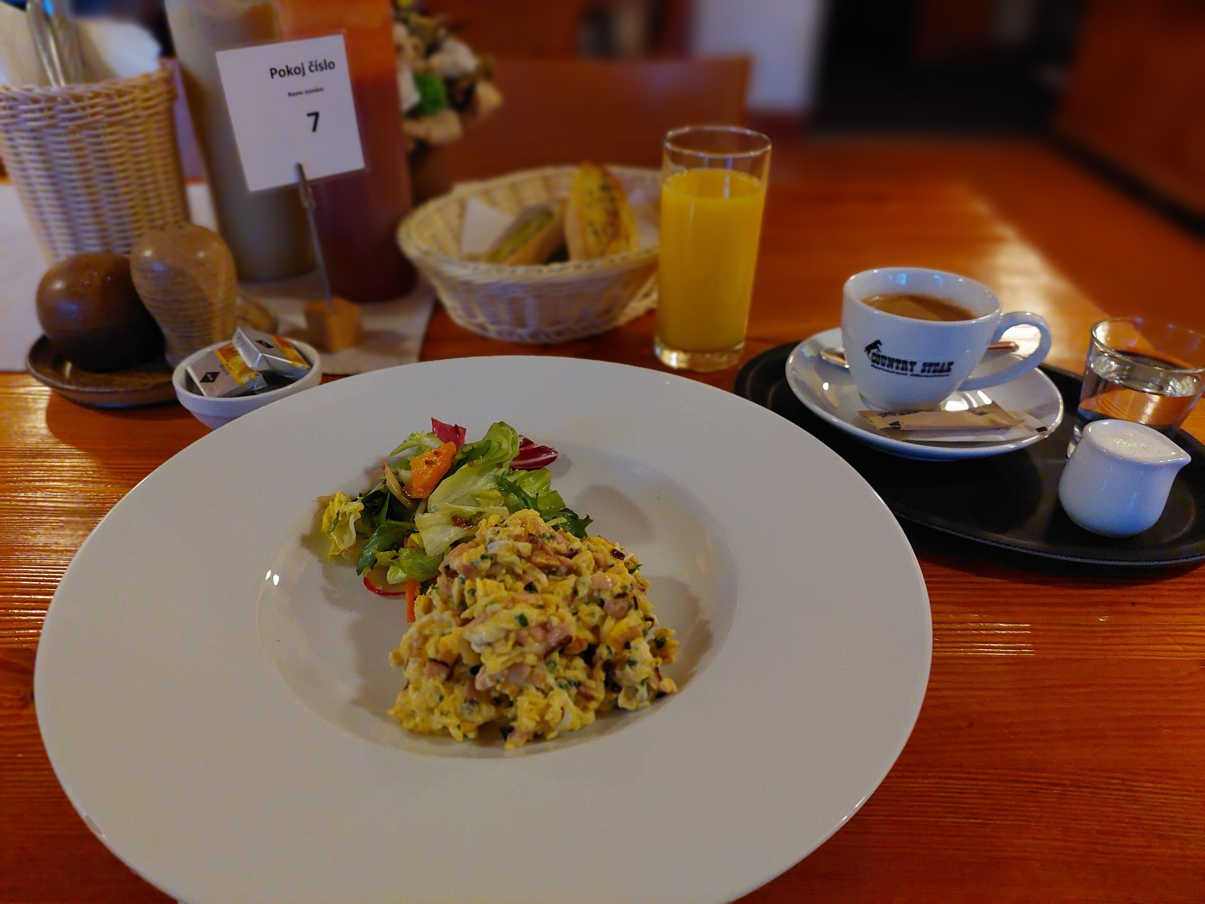 A dining table with a plate of scrambled eggs and salad, a glass of orange juice, a cup of coffee, and a small pitcher of cream.