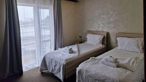 A hotel room with two beds, a window with curtains, a bedside table with a lamp, and a view of the outside. - Penzion Country Steak Restaurant (Albrechtice)