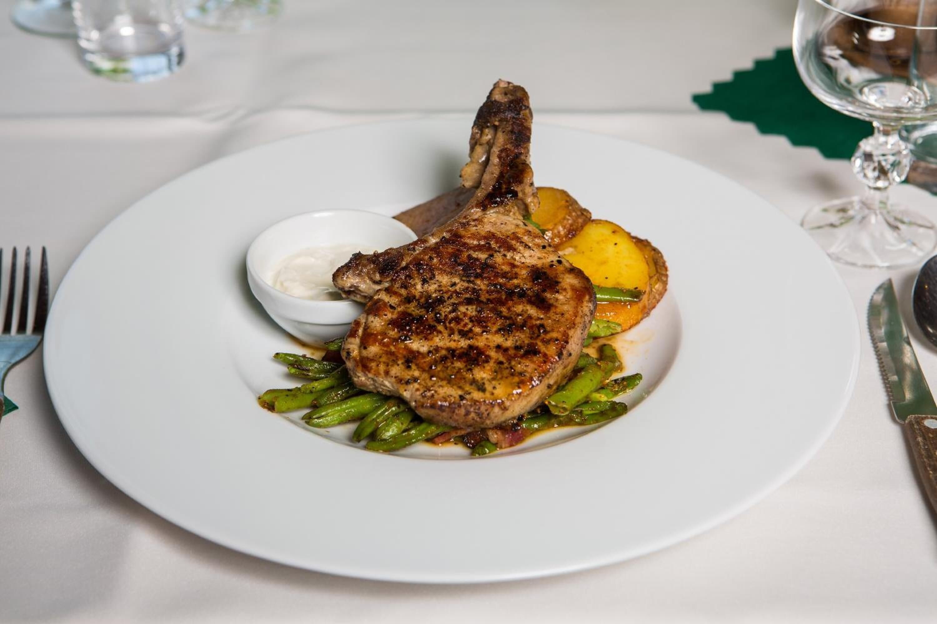 A plate with a grilled pork chop, asparagus, and a small bowl of sauce.