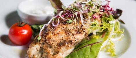 A plate with grilled chicken, mixed greens, and a cherry tomato.